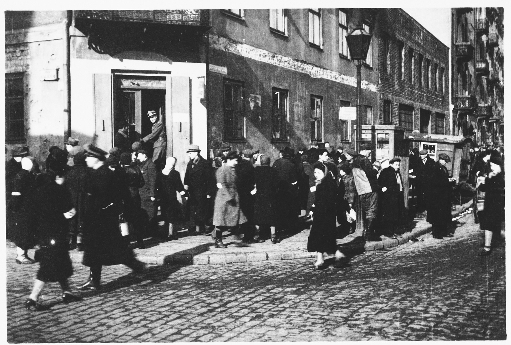 Jews wearing armbands cross a busy intersection in the Warsaw ghetto.