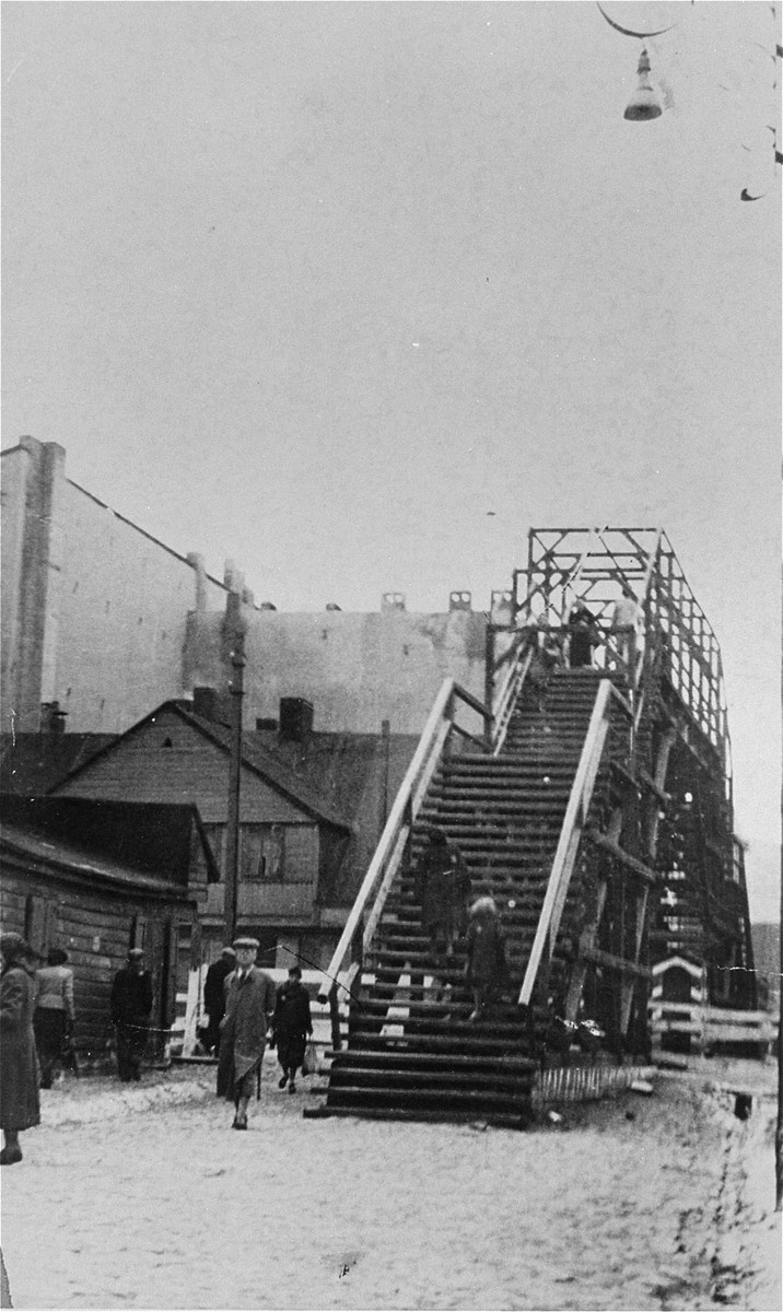 View of Lodz ghetto residents climbing the staircase to cross one of the pedestrian bridges.  The Yiddish inscription on the back of the photo reads, "The ghetto through the bridge on Marynarska Street via Aleksandrov Street - Fayfer's Alley."