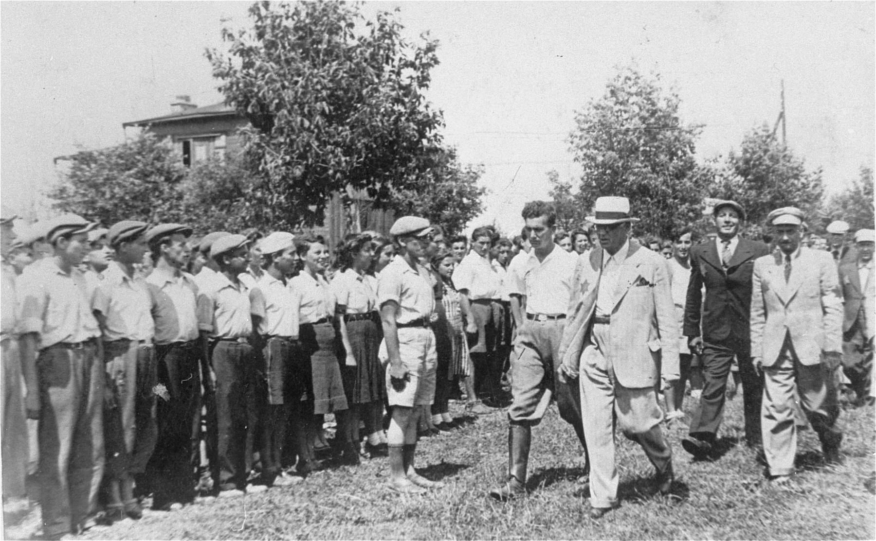 Mordechai Chaim Rumkowski, head of the Lodz ghetto Jewish council, and Leon Rosenblat, head of the Jewish police, review a group of Jewish youth during an official visit to the summer camp in the Marysin quarter of the Lodz ghetto.

Among the children pictured is Jakob Budkowski.  He was the son of Majer Szymon  Budkowski and  Szajna Zlata Lesz and was born May 13, 1927 in Lodz. He had three younger brothers; of his family, only Jakob survived.
