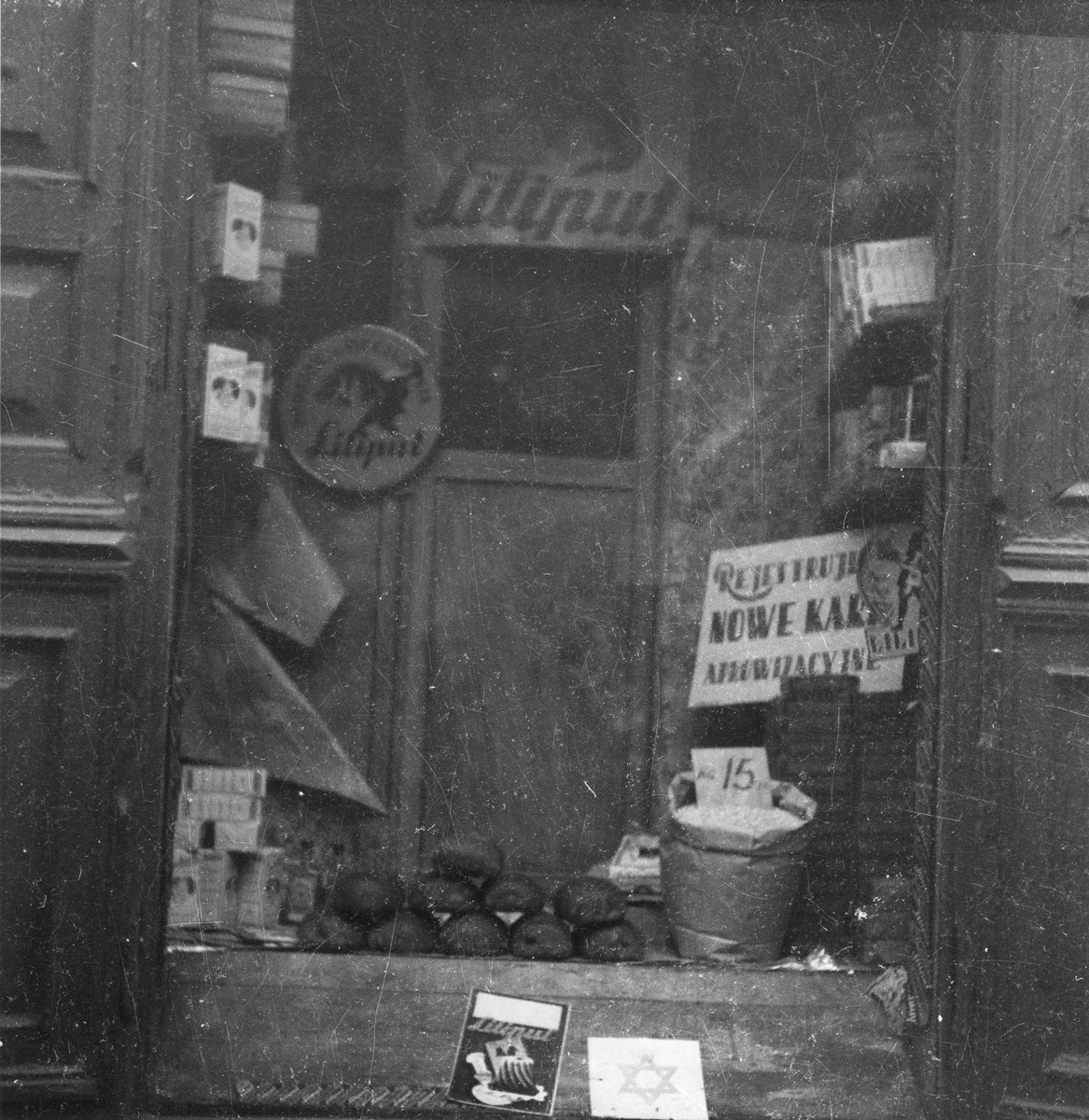 Close-up of a shop window in the Warsaw ghetto. 

Joest's original caption reads: "Fresh loaves of bread were stacked up in a window.  A bucket of beans.  Packages of Liliput baking powder.  And a sign that new 'ration cards' were being accepted here as well."