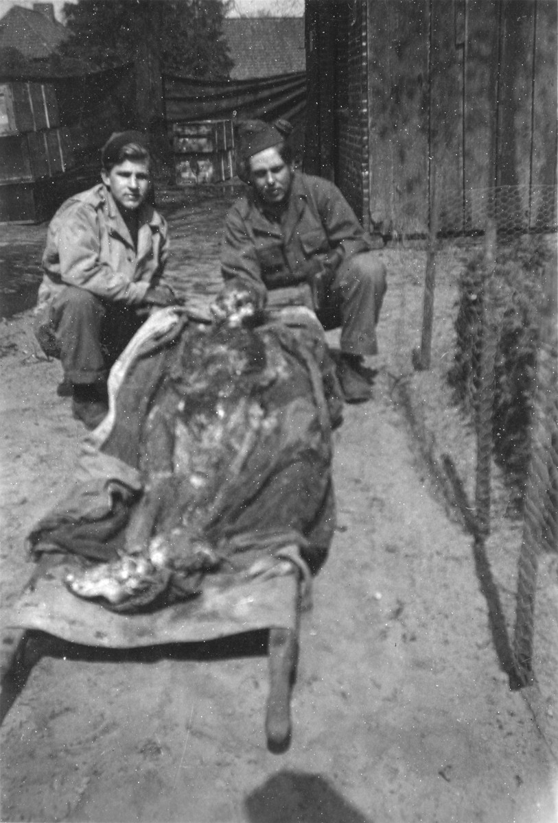 Two American soldiers kneel next to the exhumed corpse of a prisoner at Ebensee.