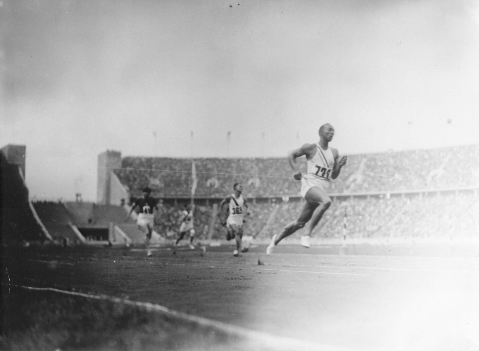 American Olympic runner Jesse Owens and other Olympic athletes compete in the twelfth heat of the first trial of the 100m dash.  

Owen won the race.  He ultimately took first place in the event, finishing the race in 10.2 seconds, a record time; however, the record was disallowed by German officials, who claimed that Owens had had the benefit of a tailwind.