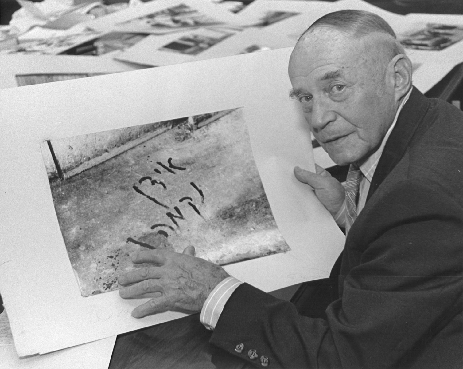 Portrait of George Kadish (formerly Zvi Kadushi), posing with a photograph he took of an inscription written by a Jew during the pogrom in the Slobodka district of Kovno in July 1941.  The Yiddish inscription reads: "Jews, avenge", and was supposedly written in blood by the victim.