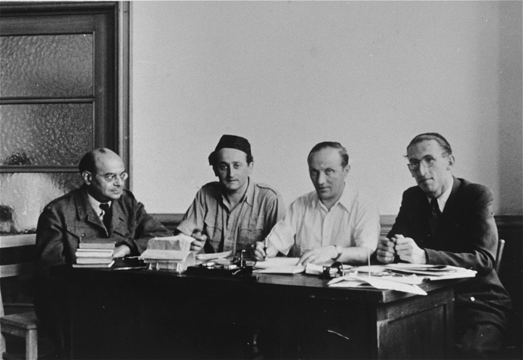 Four members of the Central Jewish Committee for the British Zone of Germany are seated in an office.

Pictured from left to right are: unknown; Rabbi Zvi Helfgott (later Zvi Asaria); Josef Rosensaft; and Rabbi Joseph Asher.