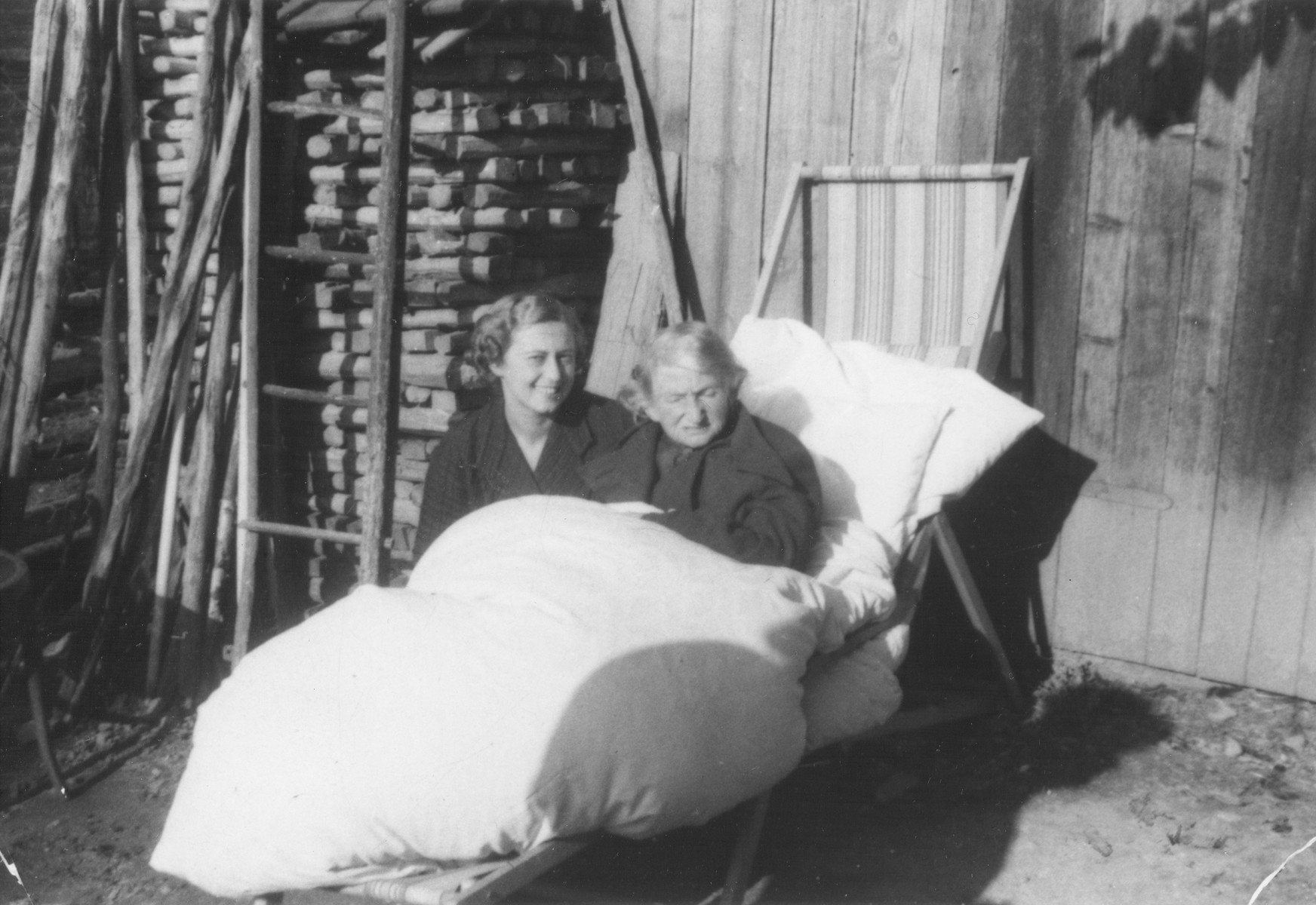 Lili Koenig poses next to her mother Sari Vermes who is sitting outside bundled up in comforters and pillows.
