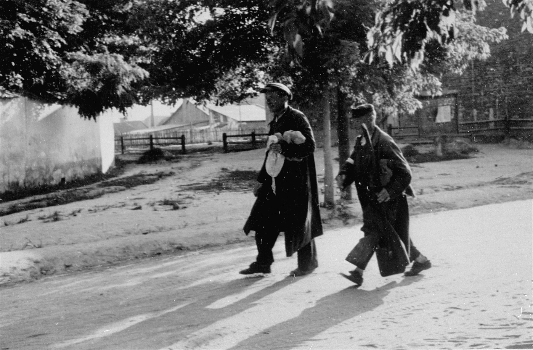 Two Jewish men who have been conscripted for forced labor, walk along an unpaved road in Konskowola.  One of them carries a shovel.