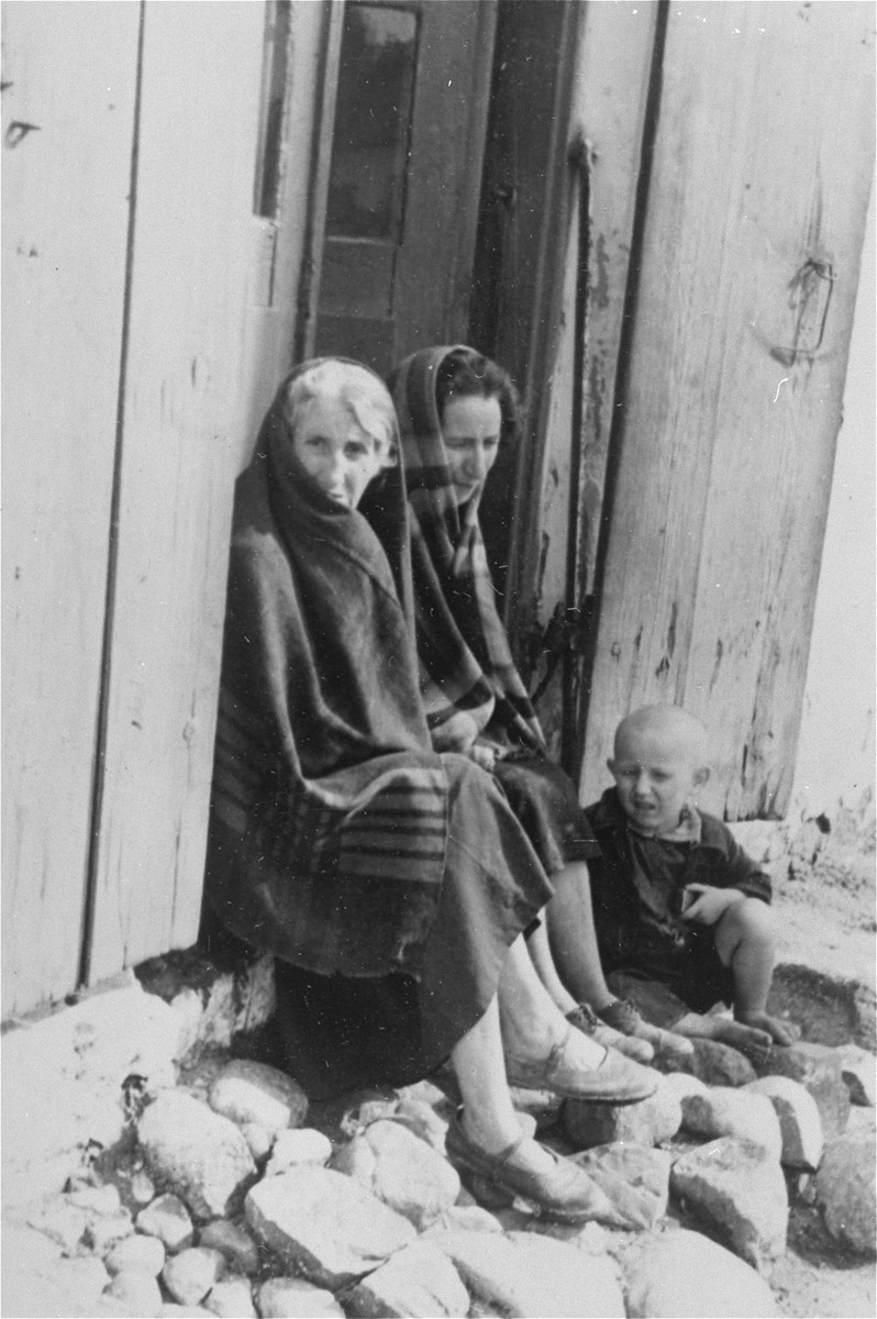 Two Jewish women and a child sit in the doorway of a wooden house in Konskowola.