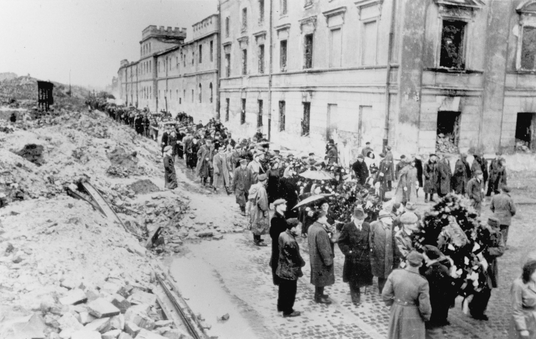 Jewish survivors carrying flags march through the ruins of the Warsaw ghetto [probably during a demonstration marking the fourth anniversary of the Warsaw ghetto uprising].