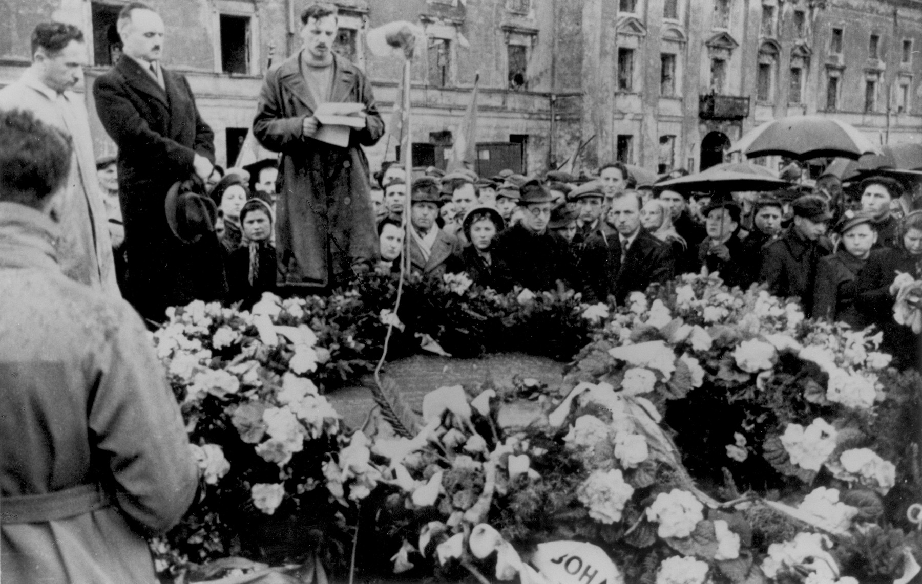 Yitzhak Zuckerman delivers a speech at a ceremony in front of the ruins of the former headquarters of the Warsaw ghetto Jewish council [probably to mark the fourth anniversary of the Warsaw ghetto uprising].

Also pictured is Dr. Adolf Berman (standing next to Zuckerman).