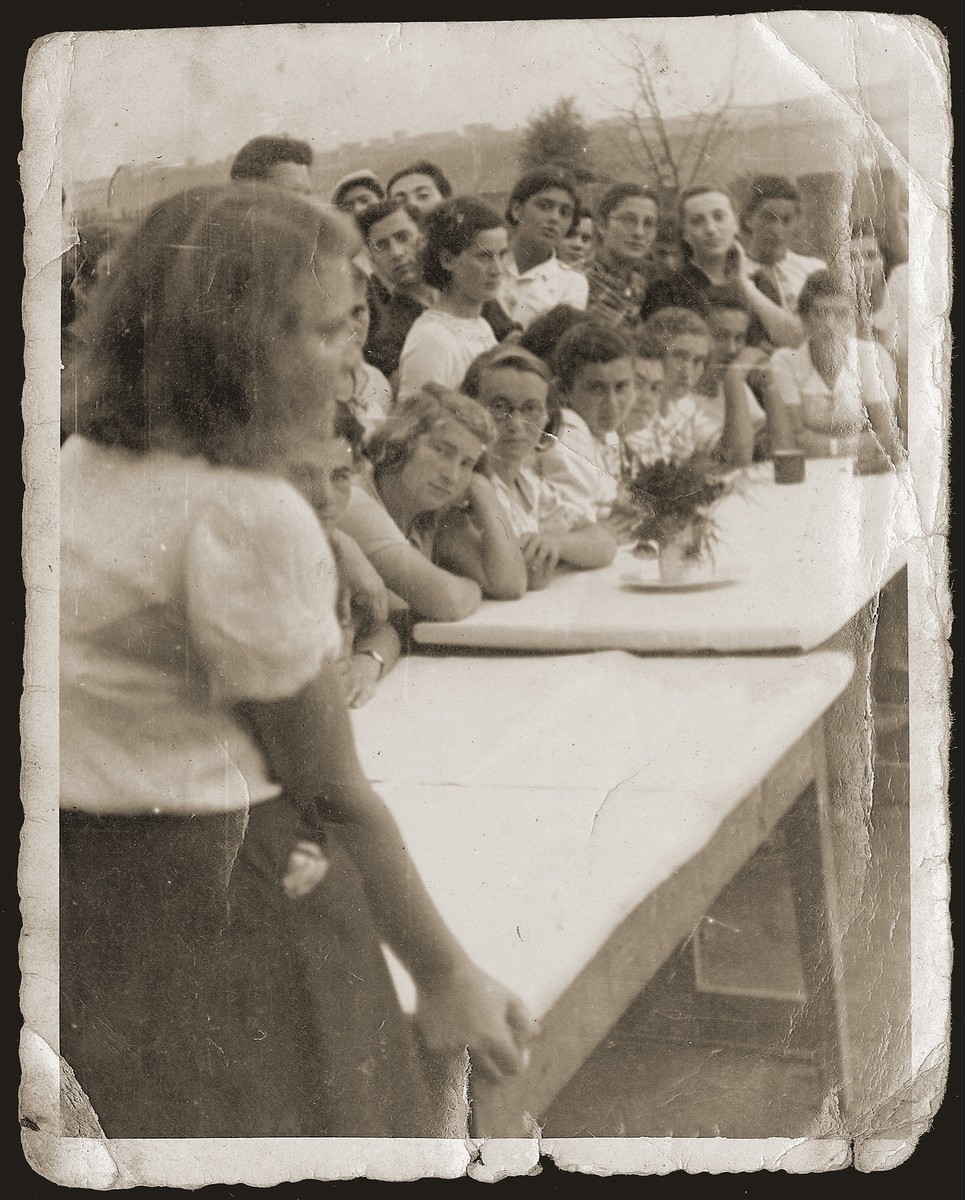 Jewish youth living at the "Farma" Zionist agricultural collective, attend a meeting. 

The "Farma" was a  plot of land between Bedzin and Sosnowiec that was allocated to the local Zionist youth movements by the Jewish Council for the growing of vegetables. The youth movements created a hachshara on the site.  Soon after, the "Farma" became the center of resistance efforts, as well as youth activity, in the ghetto.