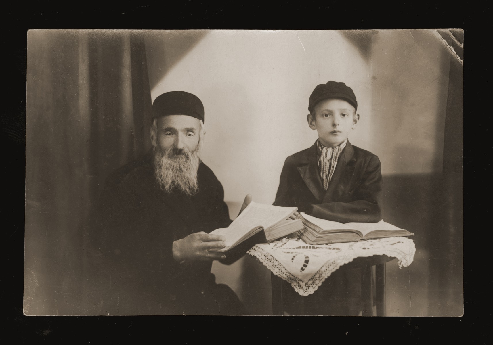Portrait of an eldery Jewish man studying a religious text with a young boy.