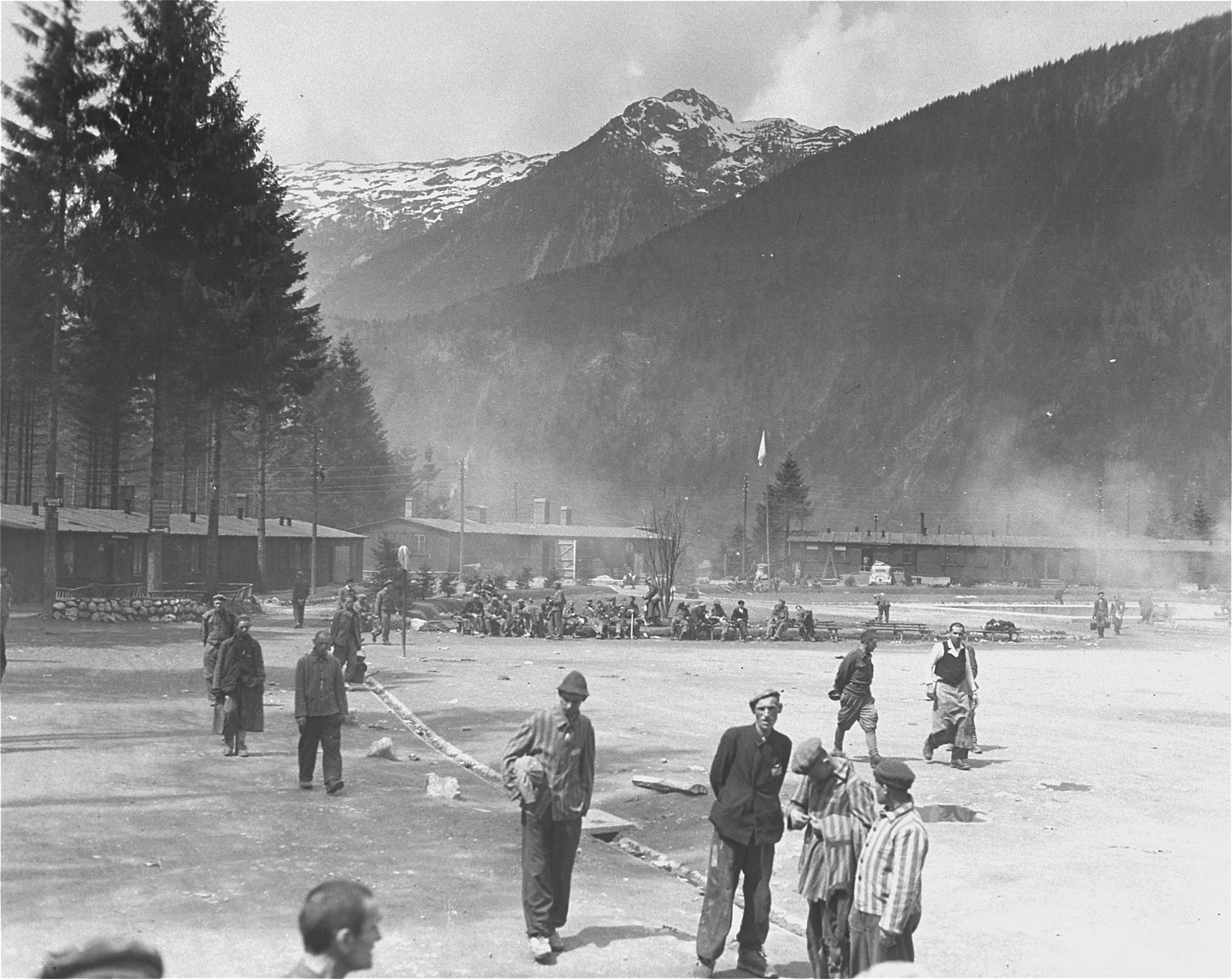 Survivors mill around the former roll call area in the Ebensee concentration camp.  

The snow-capped peaks of the Alps Mountains loom in the distance.