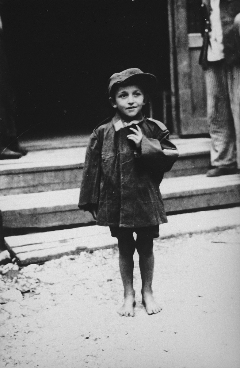 A child survivors stands in front of a barracks in the newly liberated Ebensee concentration camp.