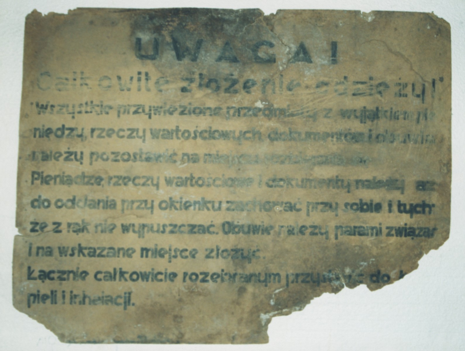 A sign in Polish from the Belzec killing center that reads, "Attention!  All belongings must be handed in at the counter except for money, documents and other valuables, which you must keep with you.  Shoes should be tied together in pairs and placed in the area marked for shoes.  Afterward, one must go completely naked to the showers."