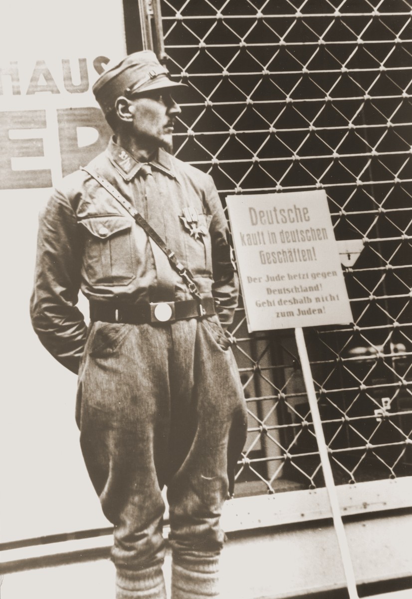 An SA member stands guard at the entrance to a Jewish-owned store during the April 1, 1933 boycott.  The sign next to him reads: "Germans shop in German stores!  The Jew is stirring up hate against Germany!  Therefore, do not go to Jewish stores!"
