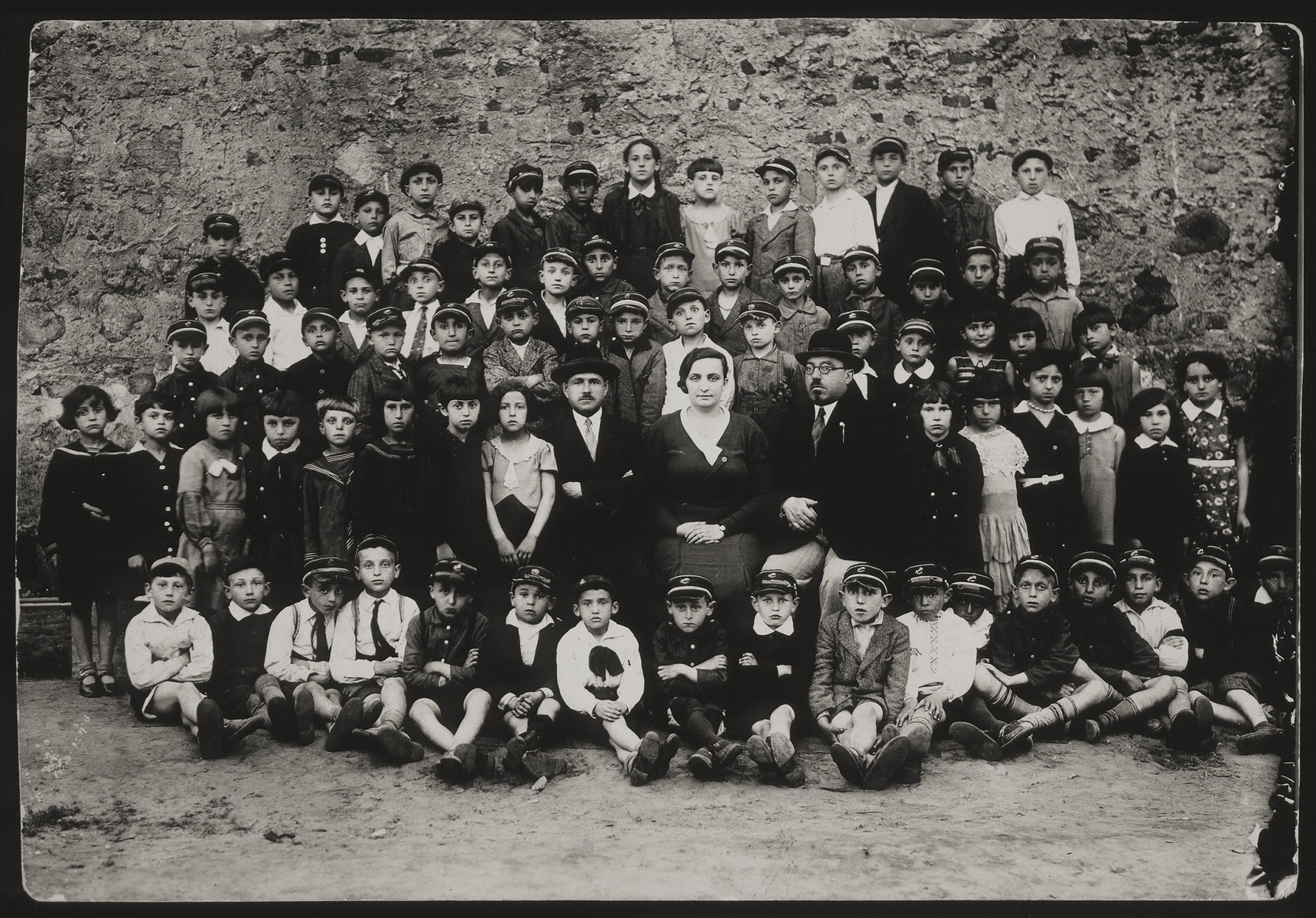 Group portrait of the elementary school in Eisiskes.

First row (sitting on the floor): Avigdor Katz (first from left), Moshe Bastunski (eighth from left) Avremele Botwinik, son of the principal (ninth from left). Second row from bottom: Rochel (far right), Rivka Dubchansky (sixth from right), Leah Tawlitski (fifth from right), Dora Kremin Dimitro (fourth from left). Sitting right of the female teacher is Shael der Lehrer.  To her left (wearing hat and glasses) is Principal Botwinik. Third row from bottom: Leibke Remz (fifth from left), Leibke Kaganovicz (Leon Kahn, sixth from left). Second row from top: Zvi Michalowski (fifth from right). Top row: Rivka Pushkin Cofnas (seventh from right). 

Dora, Leibke, Zvi, Avremel all survived the Holocaust in the forests. Rivka survived the Holocaust in Russia.  All others were murdered during the Holocaust.