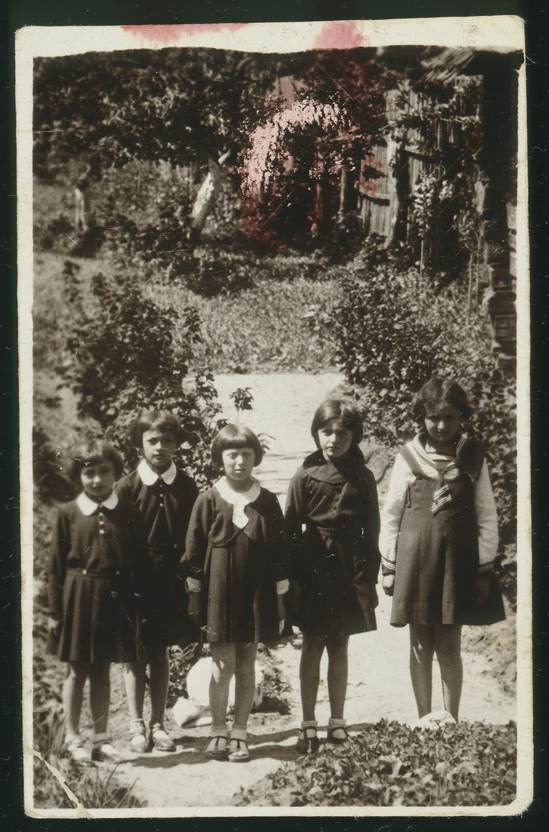 Five school girls pose in a garden in Eisiskes.  

Standing at the far right is Altke Koutsai.  Standing at the far left is Sheinele Dwinlanski and second from left is Leah Michalowski.  All the girls were murdered during the Holocaust.