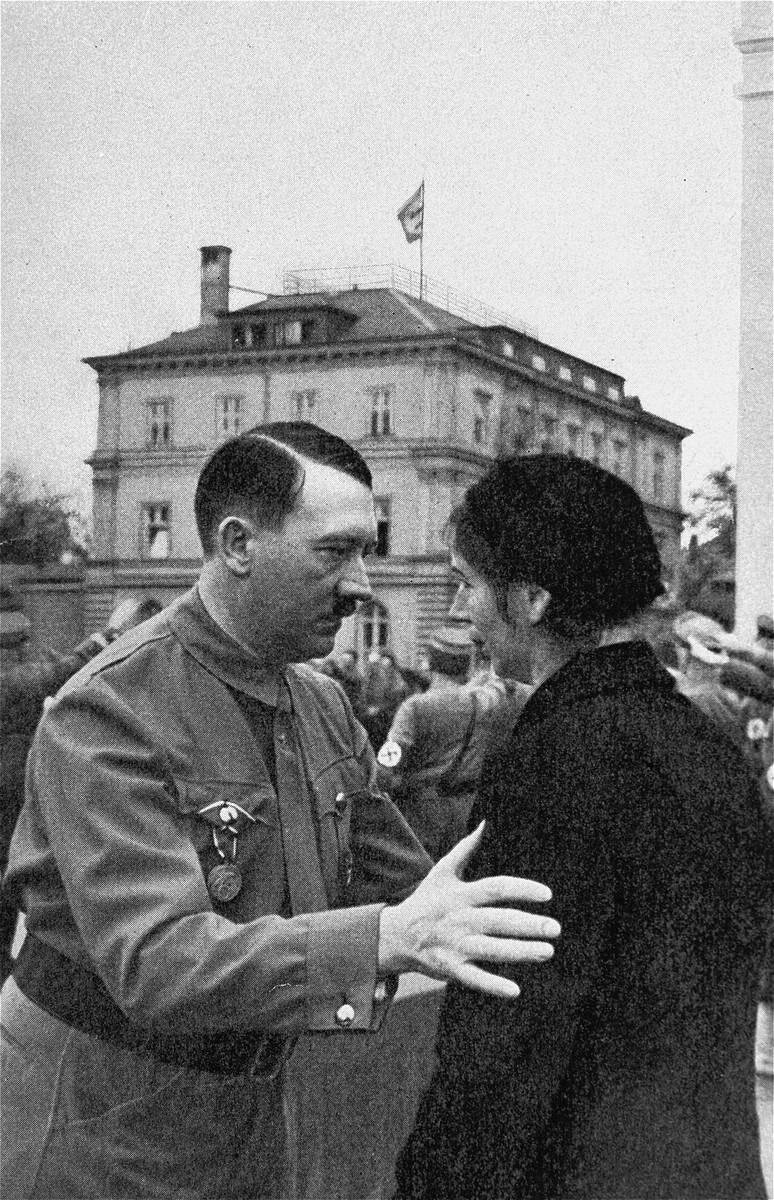 Adolf Hitler speaks to the widow of a Nazi party member who died during the 1923 Beer Hall Putsch.

In the background is the Brown House.