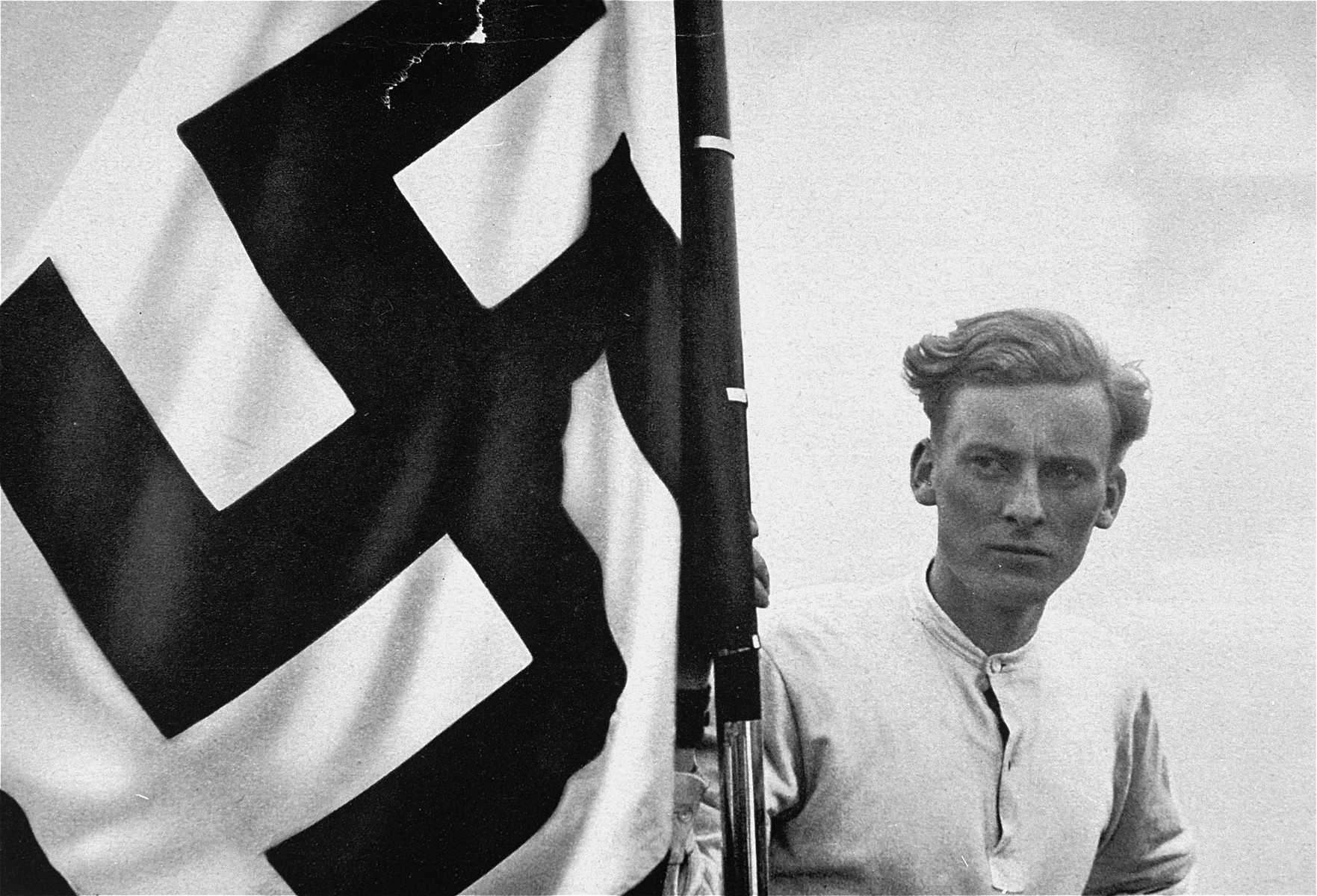 In this propaganda photograph a German youth poses with a National Socialist flag.  The German caption reads: "Our flag waves us onward."