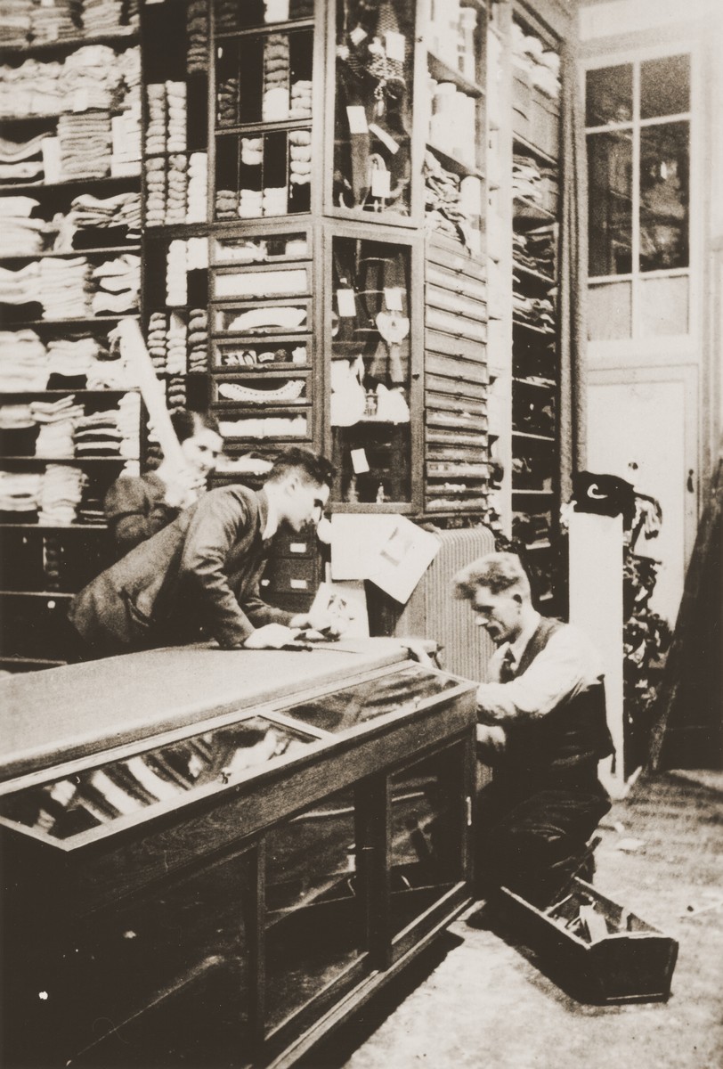 Members of the Zion family oversee last minute repairs to a counter in the family store before its formal reopening.

Pictured are Mien (left) and Zadok Zion (center) with a Dutch workman.  From August 1942, when it was confiscated, until April 1945, the Zion clothing and fabric store had been used by the Germans as a military warehouse and barracks.