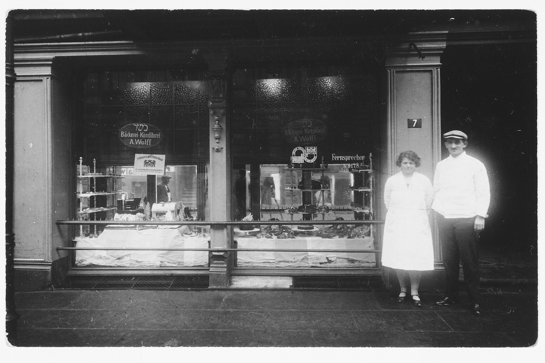 Proprietors of a kosher bakery stand in front of their store window.

Pictured are Angela Stiefel and her brother-in-law Adolf Wolf.
