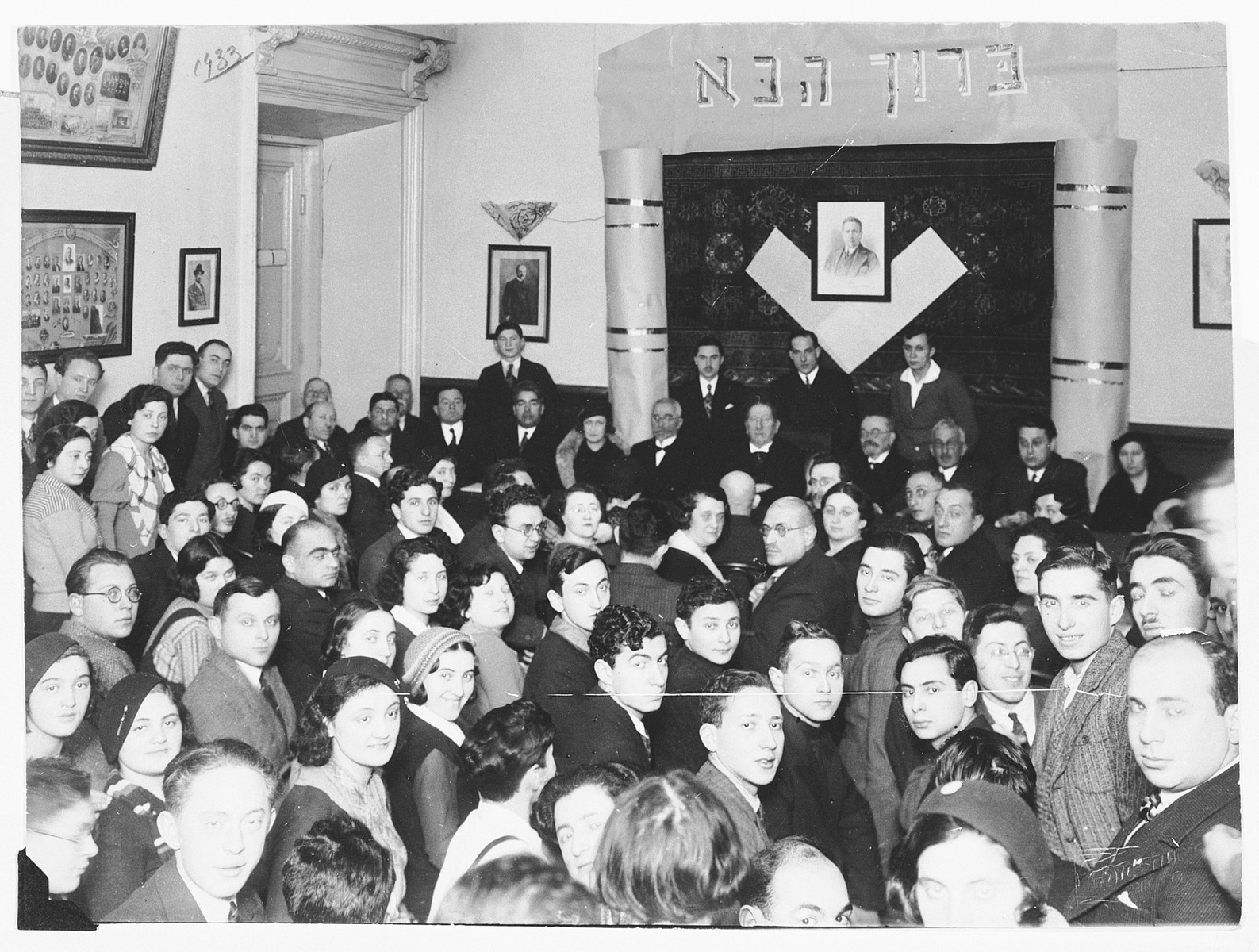 Jewish faculty and students of the Hebrew gymnasium in Vilna are gathered in the auditorium of the school during the visit of Zionist leader Nahum Sokolow.

Among those pictured is Ralph Denishevsky (beneath the Hebrew welcome sign, second from the right).