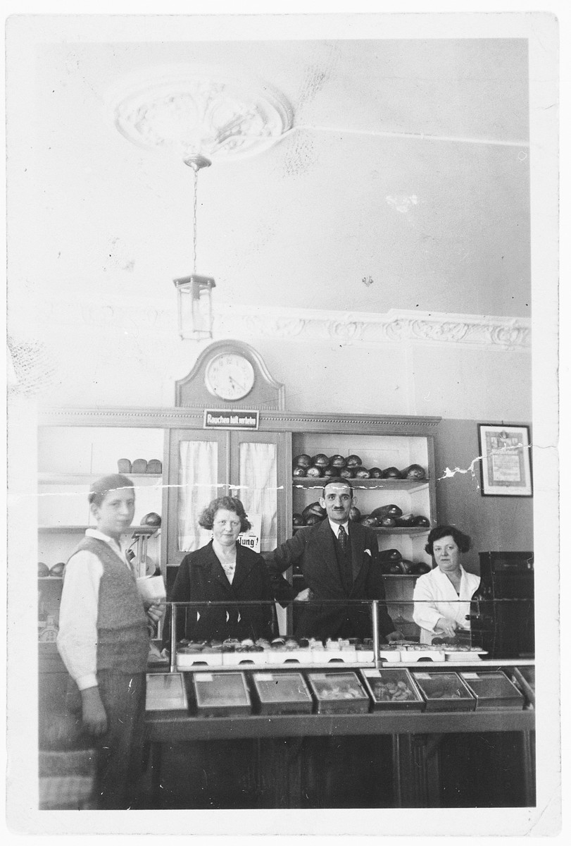 Proprietors of a kosher bakery stand next to a display counter in Hamburg.

In the center are the owners, Marta and Adolf Wolf (aunt and uncle of the donor) and Marta's sister, Angela.
