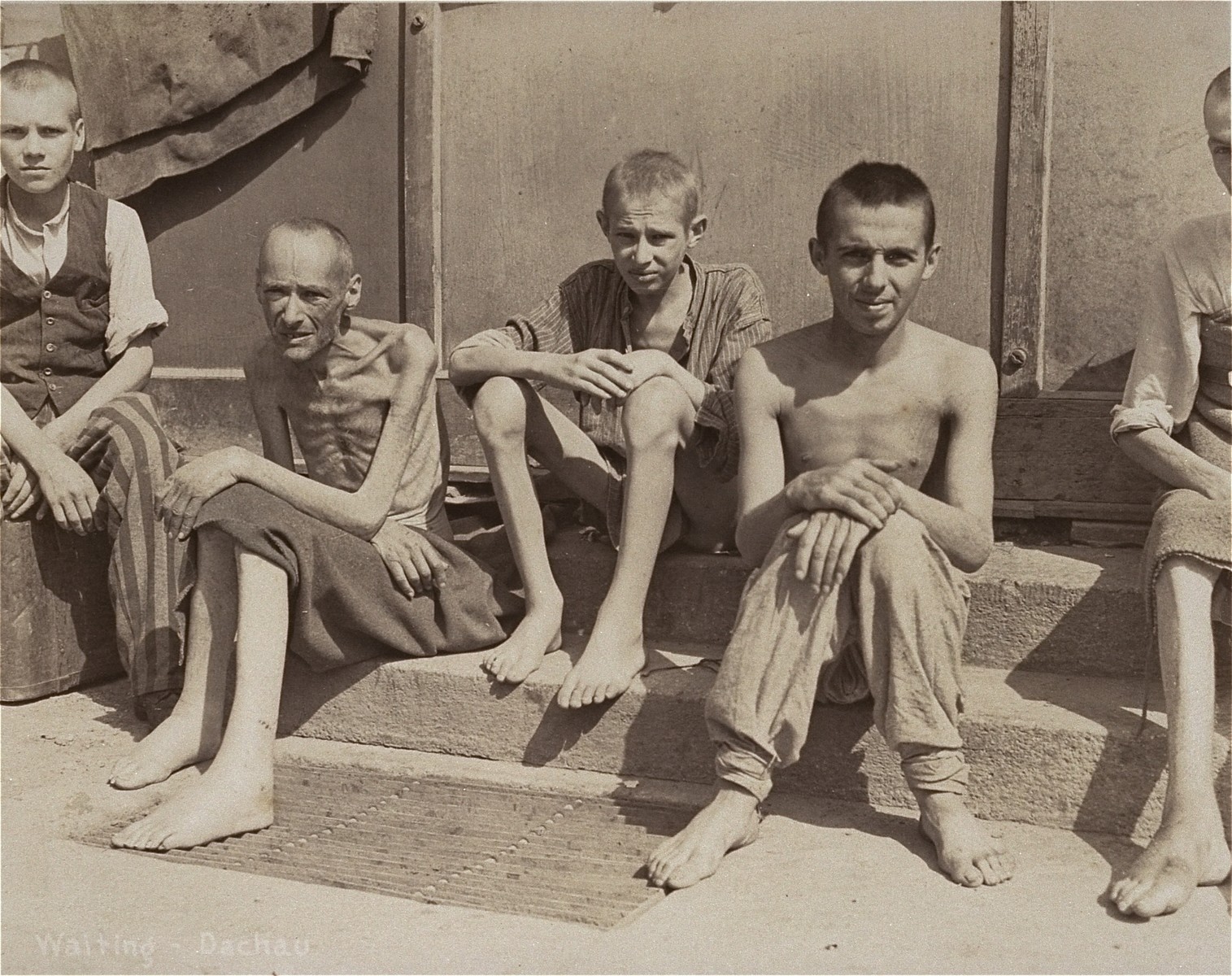 A group of emaciated survivors sit outside a barracks in the newly liberated Dachau concentration camp.