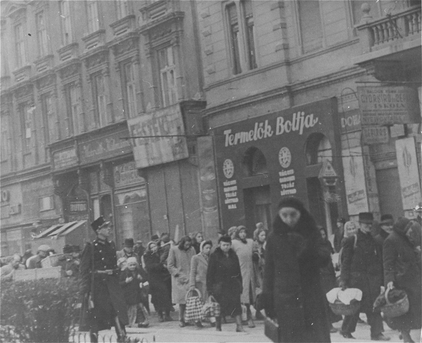 Hungarian Jews and non-Jews walk along the Jozsef Körut [Ring] in Budapest.  Many are holding shopping baskets. 

[Photographer Thomas Veres claimed in the 1990s that this image depicts Jews who were rescued from deportation by Raoul Wallenberg on their way back to the ghetto, but none are wearing the yellow star and many carry shopping baskets and appear to be waiting in line to enter a public market.]