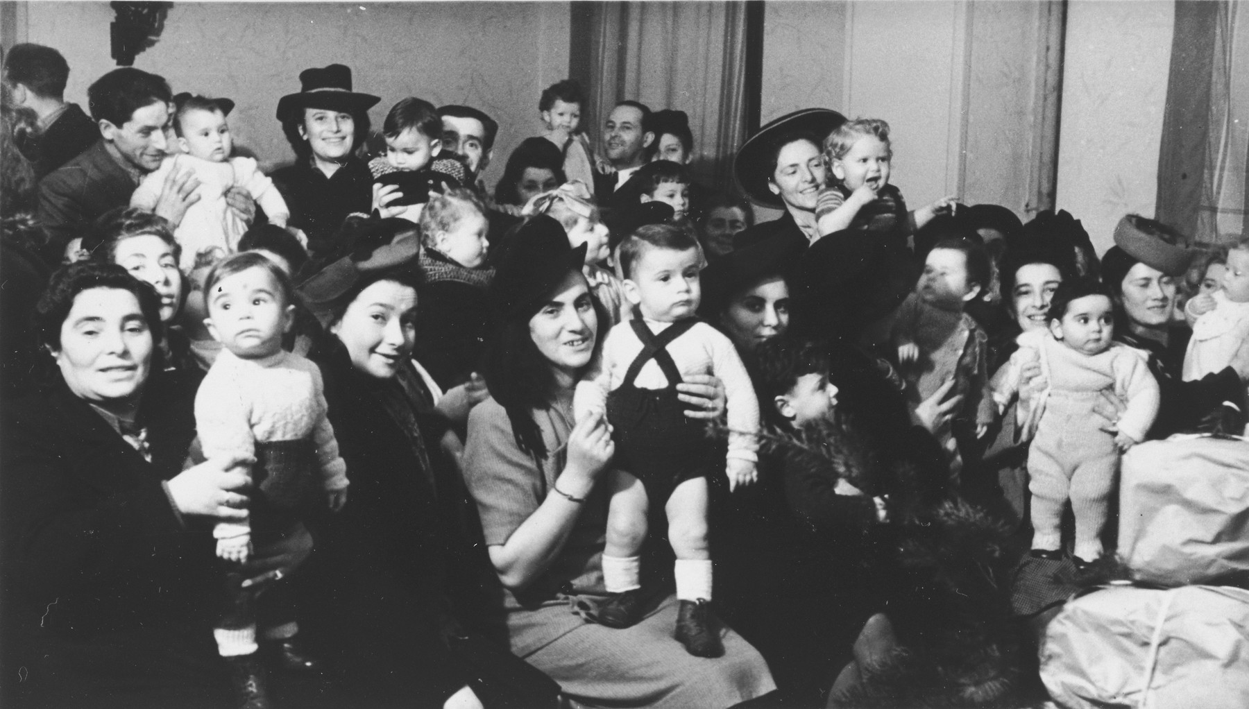 Women and children celebrate Tu B'Shvat in the Hanover DP community.

Among those pictured is Mrs. Roman Berger.  In the back center is Shimon Bornstein holding his son David. Pictured in the back of the room, center right, are Leona (Lonia) Finkler and Arnold (Abram) Finkler, holding their daugher Chava Pninah (Patricia) Finkler Friedland.