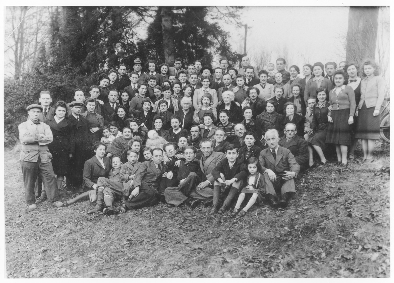 Group portrait of German Jewish refugees living in Belgium who were forcibly resettled to Bilzen after the German invasion in anticipation of their being deported back to Germany.

Among those pictured are Gisele Soldinger (second from the right), Ida Soldinger (standing on the left), Hinda Rose Soldinger (fourth row from the front, third from the right) and Edgar David Soldinger (top row, center).   

Also pictured is Mendel Szydlow standing in the last row, 8th person from the right holding his infant son Werner. His wife Berta Szydlow- Sieradzki is the 2nd person to the right of him. Mendel was deported on transport X and murdered in Auschwitz. His wife and son survived the war in hiding.

Also pictured are  Menasche Steinhardt, his wife Eidla Edith Steinhardt-Safier and their son Harry Henri Steinhardt. Menasche is standing on the second row standing, second from the left, only his head visible behand the person with the darker cap. His wife with their son on her lap is sitting two persons to his right.