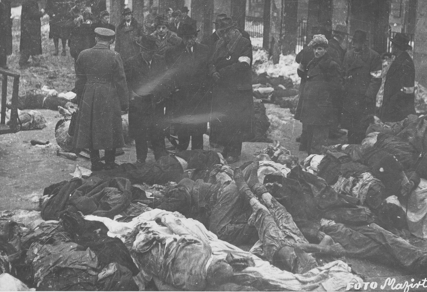 Members of the Commission for the Investigation of Nazi and Arrow Cross Atrocities examine the bodies of Jews in the courtyard of the Dohany Street Synagogue.

During the last few months of the war in Hungary, the Nyilas (Arrow Cross) exploited the anarchic conditions in the areas still under their control to continue their excesses against the Jews.  This was particularly true in Budapest, despite the fact that the Soviet army had completely encircled the city by December 27, 1944.  The reign of terror that had begun with Szalaszi's assumption of power on October 15, 1944, went almost completely unchecked after the beginning of the Soviet siege on December 9.  Gangs of armed Nyilas--mostly teenagers--roamed the city hunting for Jews in hiding.  They searched them out in hospitals, shelters, homes outside the ghetto, in the International Ghetto, and in the large ghetto.  After robbing the Jews of their remaining valuables, the Nyilas shot them on the spot or marched them to the banks of the Danube, where they shot them, and threw their bodies into the river.  A large number of Jews who were murdered in the ghetto were buried in mass graves in the courtyard of the Dohany Street Synagogue.

The most horrific of these attacks occurred on the Pest side of the capital, at the two Jewish hospitals located on Maros and Varosmajor streets.  The Maros Street hospital, which had operated under the protection of the International Red Cross during the German occupation, was attacked on January 11, 1945.  After the initial melee, during which Nyilas gang members wantonly destroyed hospital equipment, threw patients out of their beds and trampled them, and murdered staff members, survivors were ordered to dig a mass grave, remove and bury the bodies.  They were then shot and buried in the grave themselves.  Only one nurse survived of the 92 people that were in the hospital at the time.  Three days later, on January 14, the hospital on Varosmajor Street was attacked, resulting in the deaths of 150 patients and medical staff.  These manhunts and massacres continued unabated until the liberation of Budapest in April.  [R. Braham, "The Politics of Genocide," vol. 2: 995-1007]