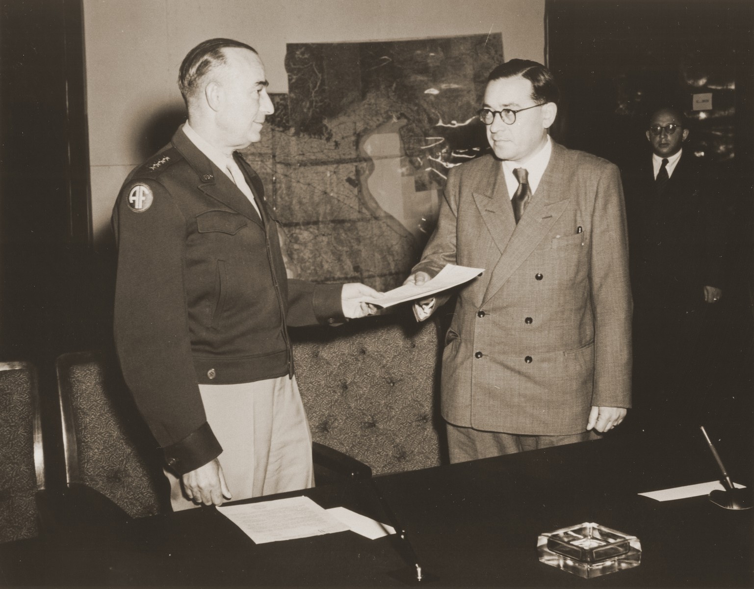 General Joseph McNarney, Commander of the American army of occupation in Germany, hands Dr. Samuel Gringauz, Chairman of the Central Committee of Liberated Jews in the U.S. Zone of Germany, the signed Charter of Recognition, whereby the American army acknowledged the Central Committee as the official representative body of Jewish DPs in the American Zone of Germany.

Pictured at the far right is Boris Pliskin.