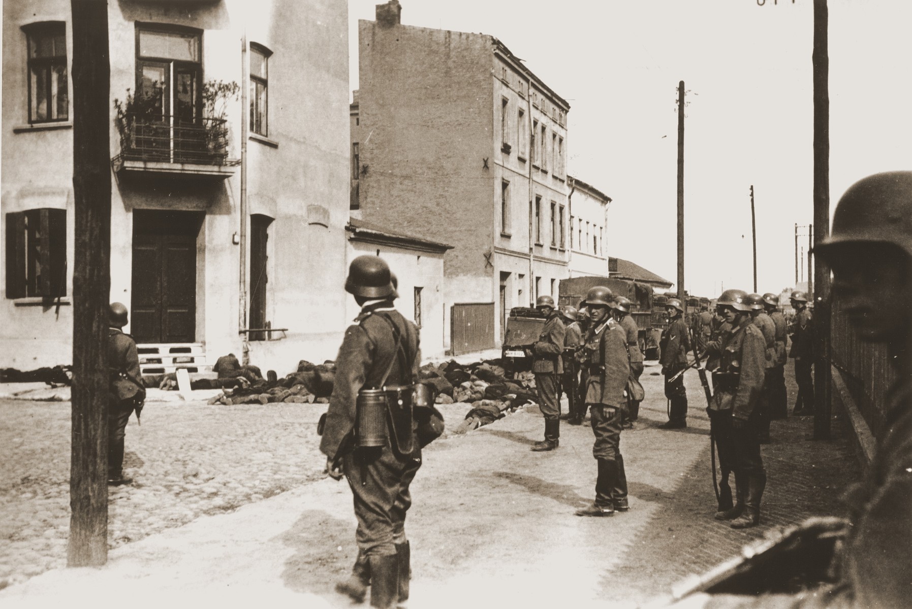 German soldiers stand guard on a street in Czestochowa, where the bodies of Jewish men they have shot, lie on the pavement.  

One photograph from an album belonging to a member of a Wehrmacht machine gunners' unit, which was found after the war by Lorenzo Hawkins (the donor's grandfather), an American serviceman in Company B, 56th Armored Engineer Battalion.
