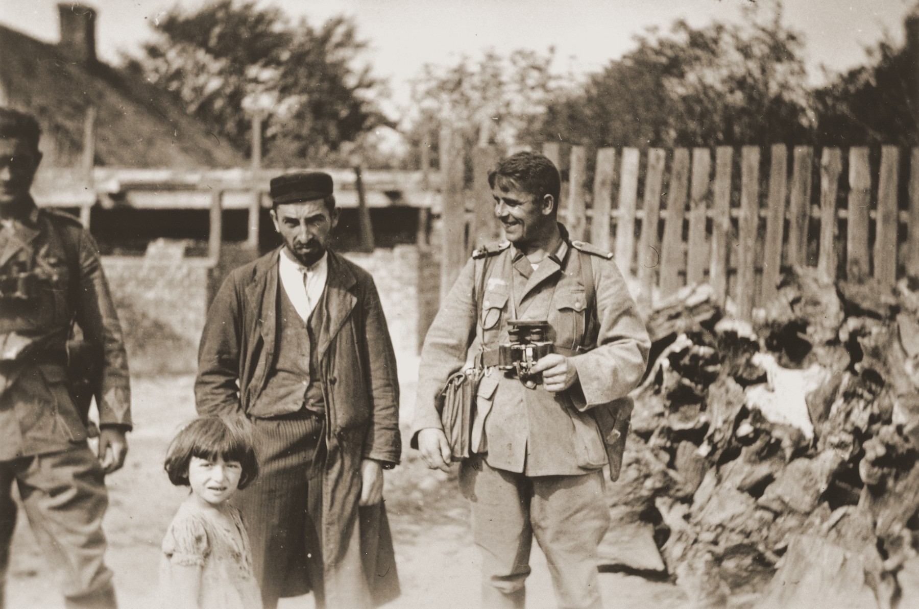 A German soldier with a binoculars laughs at a Polish Jew, who stands with his young daughter. 

One photograph from an album belonging to a member of a Wehrmacht machine gunners' unit, which was found after the war by Lorenzo Hawkins (the donor's grandfather), an American serviceman in Company B, 56th Armored Engineer Battalion.