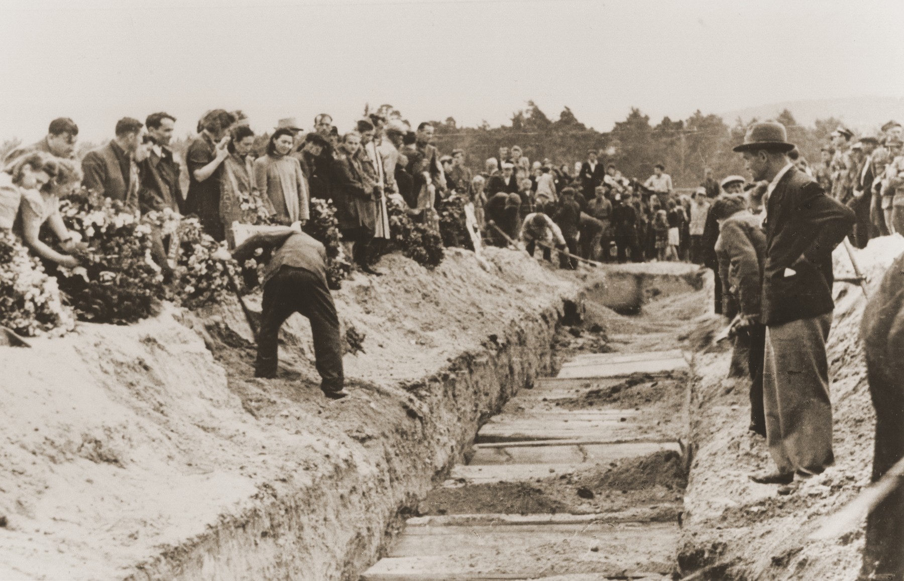 Mourners and local residents shovel dirt into the mass grave of the victims of the Kielce pogrom during the public burial.