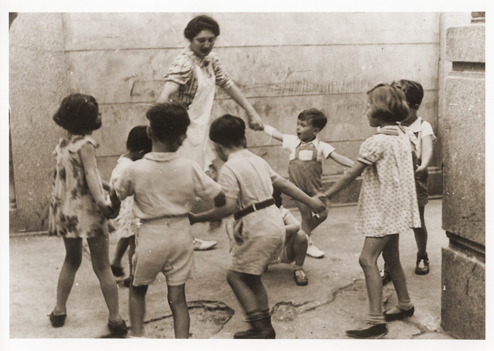 A teacher leads a group of young children in a circle dance at the Shanghai Jewish Youth Association School.

Among those pictured is Wolfgang Gotthelf (far right, partially hidden from view).  His aunt is the teacher.