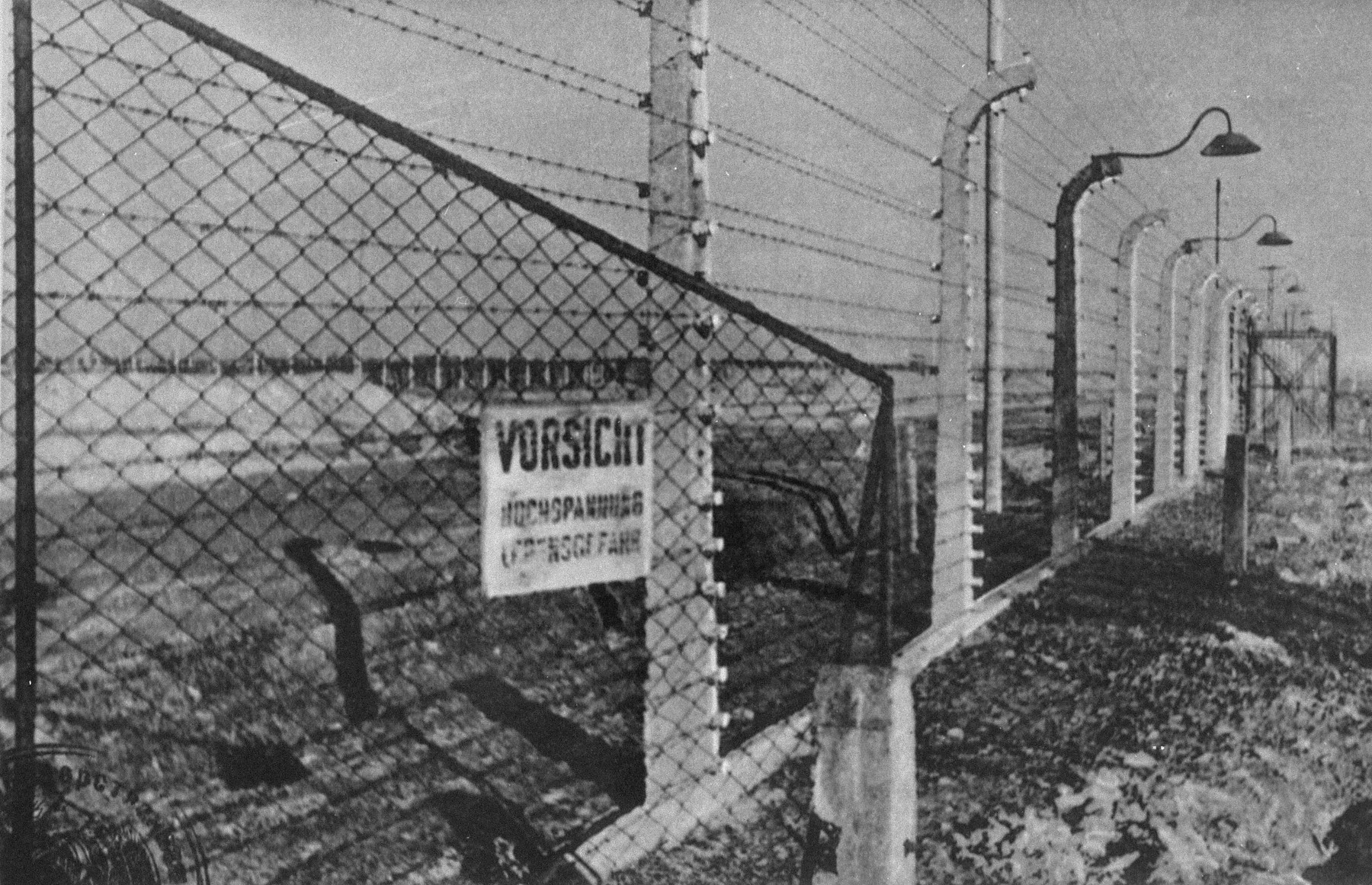 A view of the electrified fence in Auschwitz.  The sign reads, "Caution! High voltage. Danger to life."