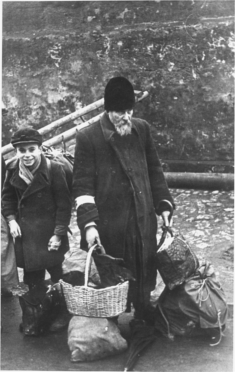 An elderly man and child who have been rounded-up for deportation wait with their luggage at an assembly point in the Krakow ghetto. 

[detail of w/s 02144]