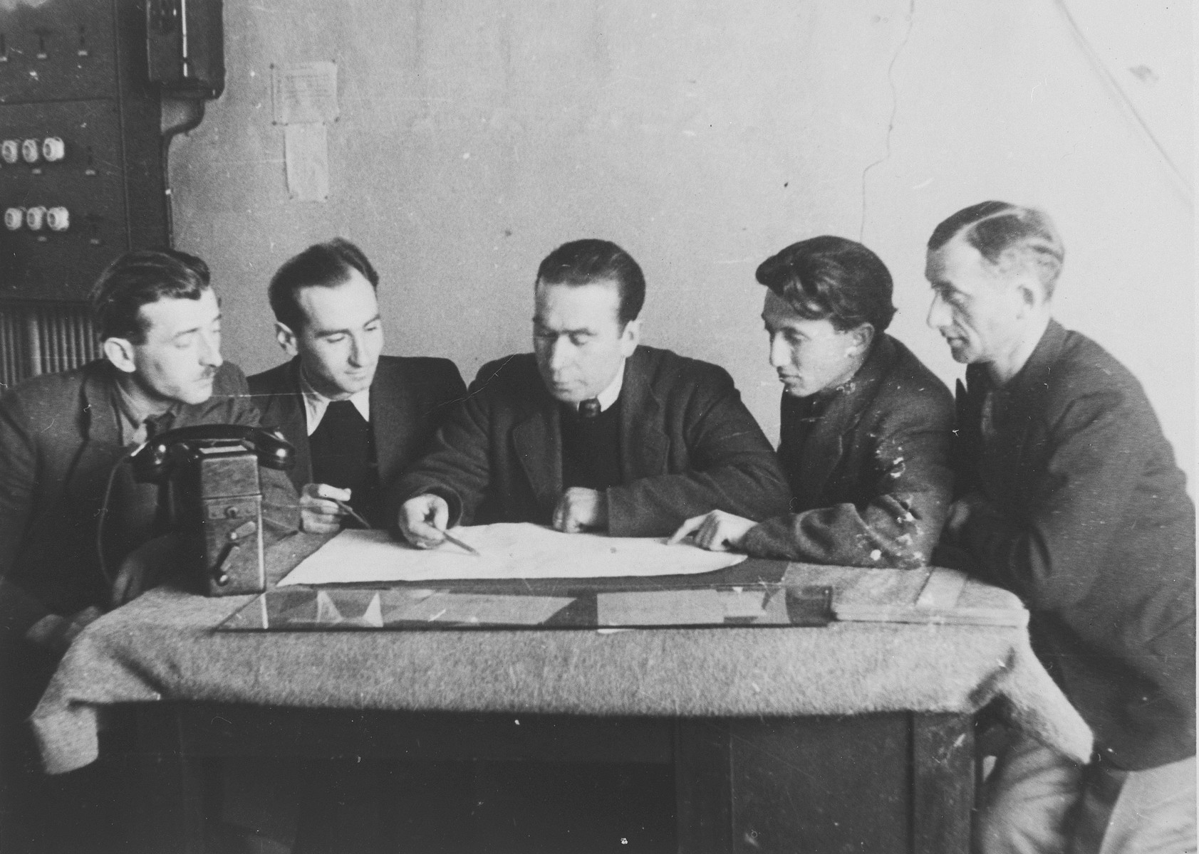 Edward Cittrons, director of ORT in Neu-Ulm, and four other men examine some plans on a table in his office.