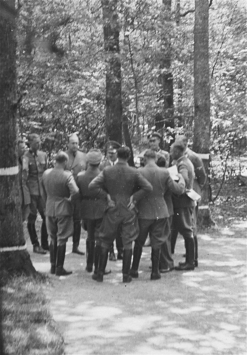 Adolf Hitler talks to other Nazi military officials at a wooded location.