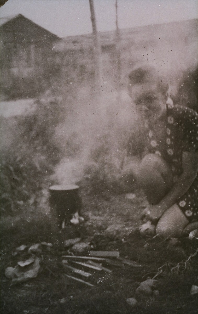 A woman prisoner in Gurs cooks on an open fire in Ilot L.  This photograph was shot secretly by Alice Resch-Synnestvedt during her stay in Gurs as a delegate of the American Friends Service Committee.