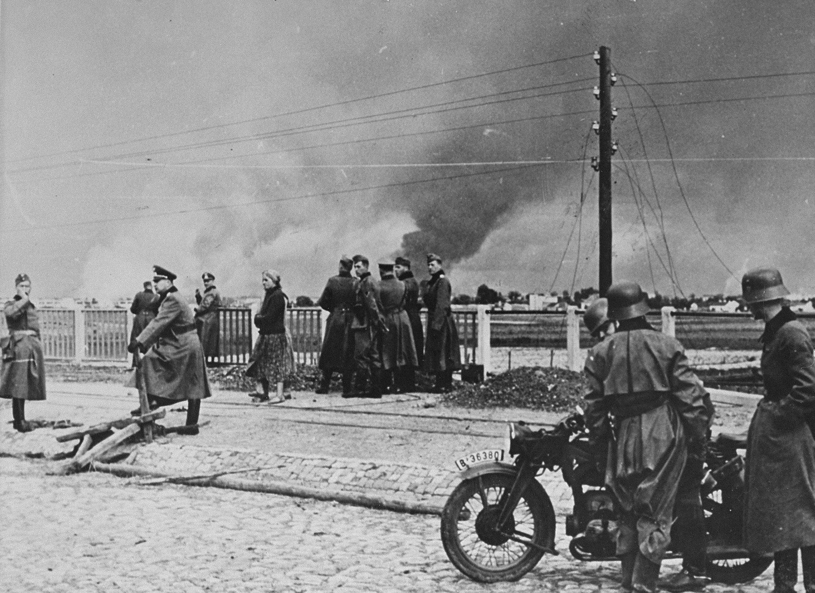 German troops and Polish civilians stop on a bridge on the outskirts of Warsaw, as smoke rises from the burning city.