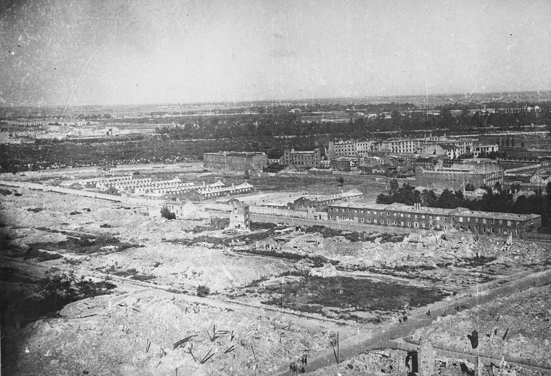View of the ruins of the Warsaw ghetto.  

Pictured in the middle, surrounded by high wall with watch towers, is the west side of the Gesiowka prison.  The Jewish cemetery on Okopowa Street is visible in the background on the left behind Gesiowka concentration camp.