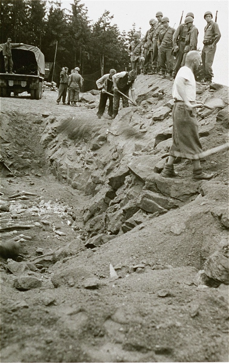 American soldiers look on as Austrian civilians bury the bodies of former inmates in a mass grave in the Mauthausen concentration camp.
