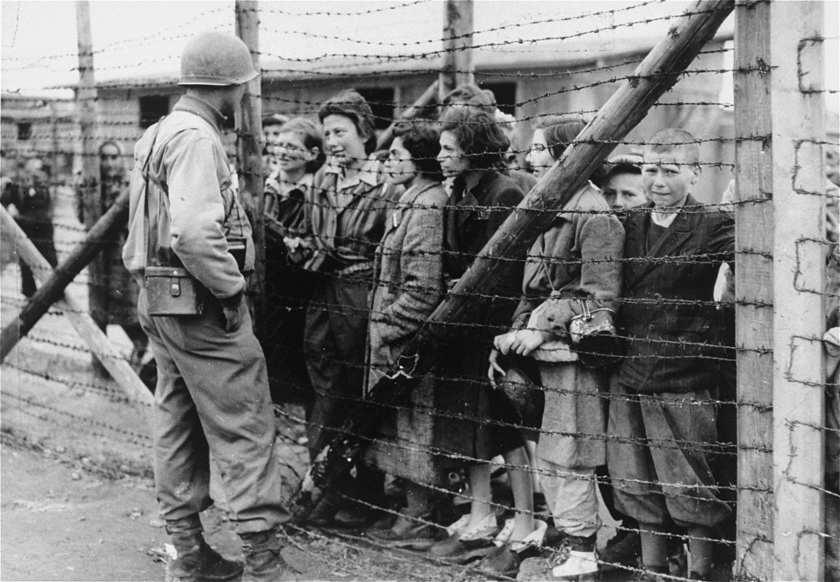 Women and children survivors in Mauthausen speak to an American liberator through a barbed wire fence.