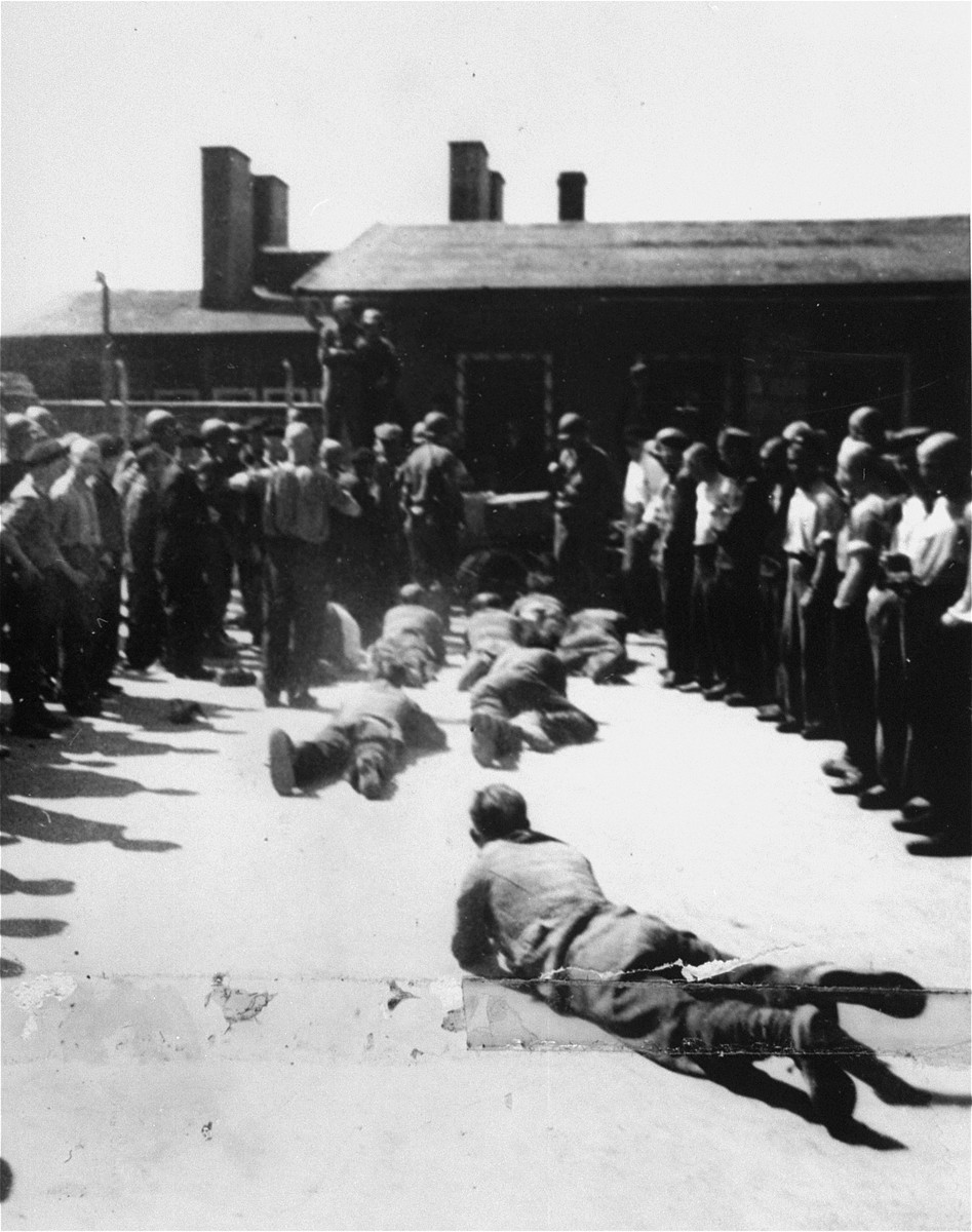 Survivors and American soldiers watch as former SS guards are forced to crawl along the ground at the Mauthausen concentration camp.