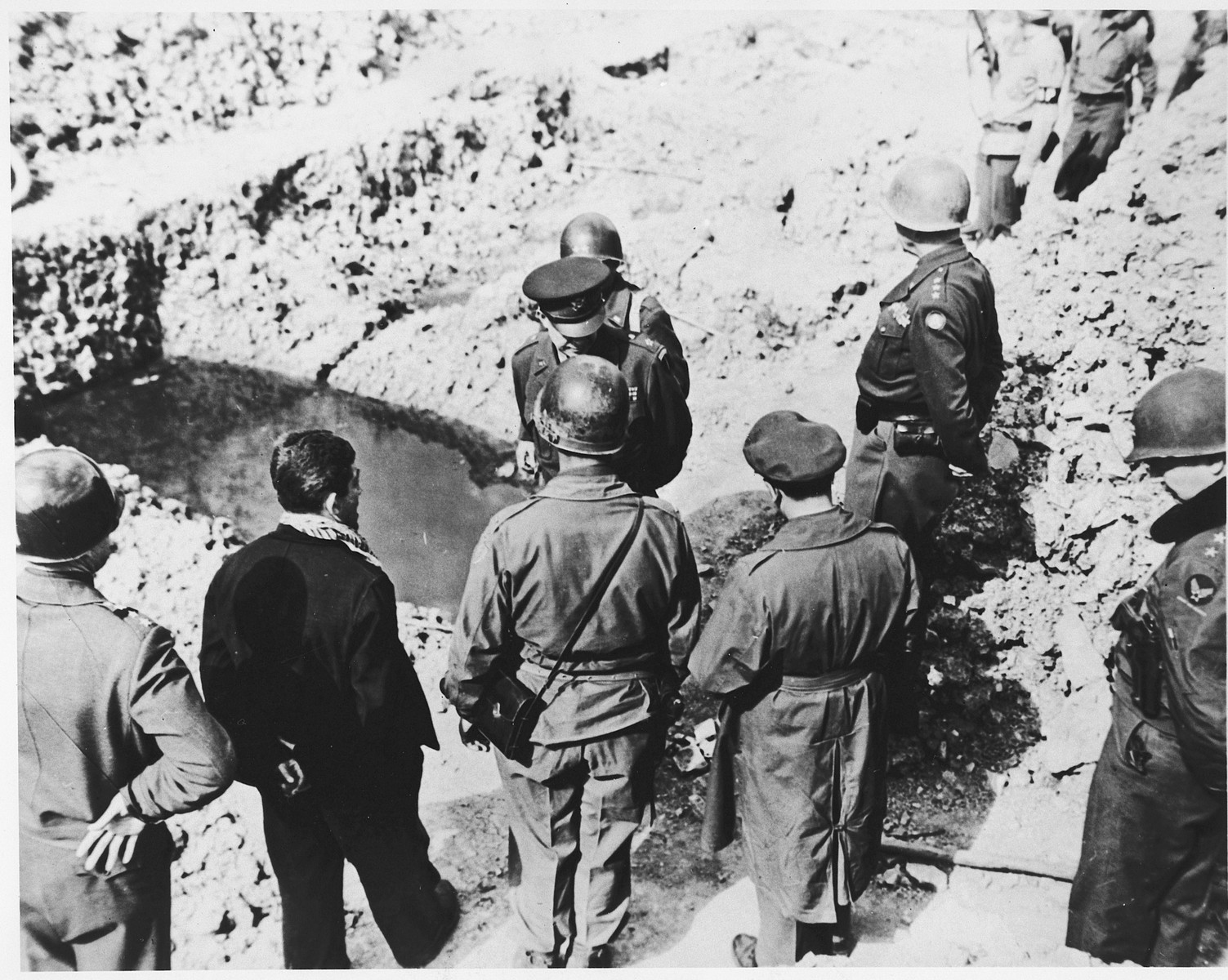 High-ranking U.S. Army officers examine a mass grave in the newly liberated Ohrdruf concentration camp.

Among those pictured are Generals Dwight D. Eisenhower, George Patton, Omar Bradley and Manton Eddy.  Also pictured is Jules Grad, correspondent for the U.S. Army newspaper, "Stars and Stripes".  Also pictured is Ignaz Feldmann (back to camera, wearing a dark coat and a scarf) . He was a survivor of  Westerbork, Terezin, Auschwitz, and Ohrdruf camps.   He was also a player on the famed Hakoah Vienna soccer teams of the 1920s and 30s.
