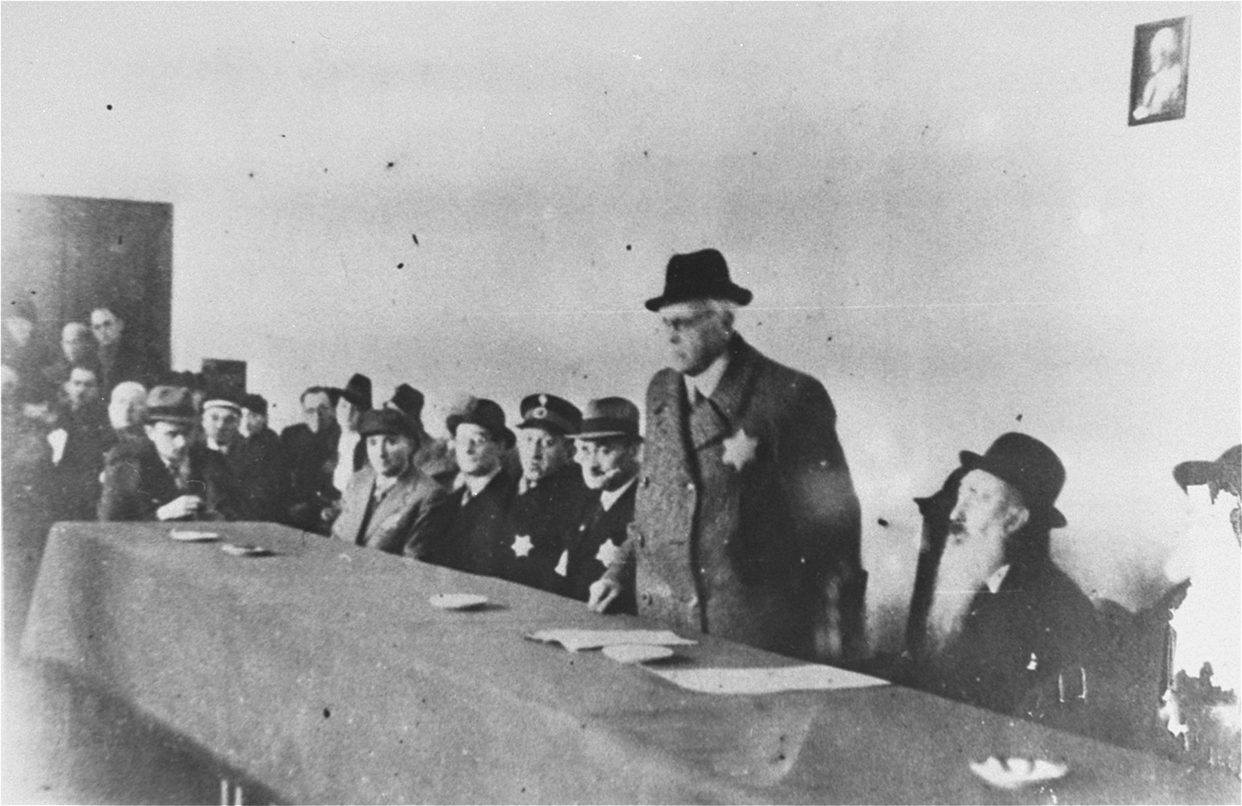Mordechai Chaim Rumkowski delivers a speech at a meeting of Lodz ghetto officials.  

Among those pictured are: Rabbi Josif Fajner (second from the right), Dr. Leon Szykier (fifth from the right, wearing a uniform cap).