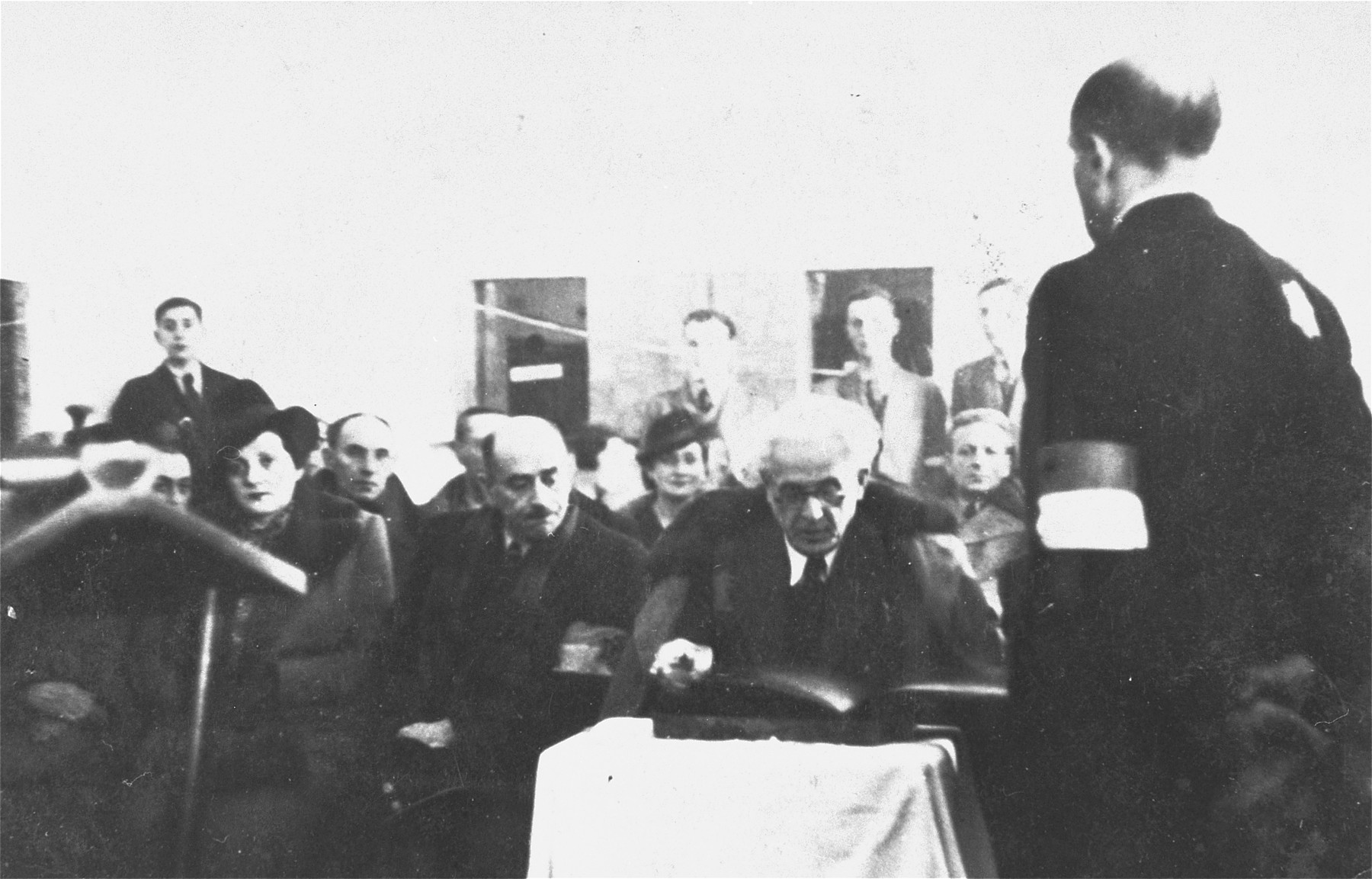 Jewish council chairman Mordechai Chaim Rumkowski (center), views a presentation album at a ceremony in the Lodz ghetto.  

Pictured in front from right to left are: Dr. Leon Szykier; Mordechai Chaim Rumkowski, Leon Rozenblat and Helena Rumkowska.